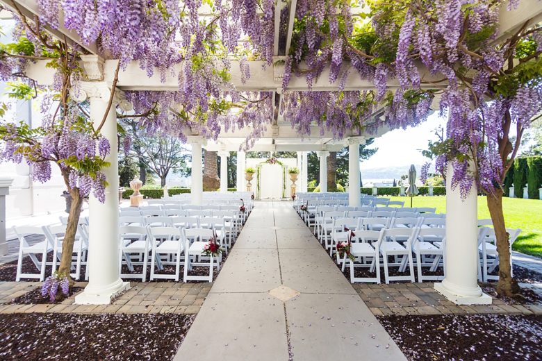 Ceremony venue with white chairs and wisteria on a pergola overhead