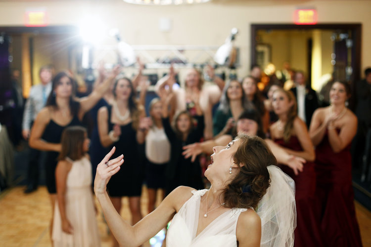 Bride throwing bouquet over shoulder to a group of women and girls in formal wear