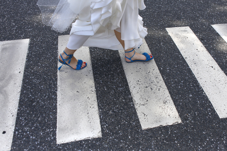 View of feet of bride wearing blue flat sandals walking across a crosswalk