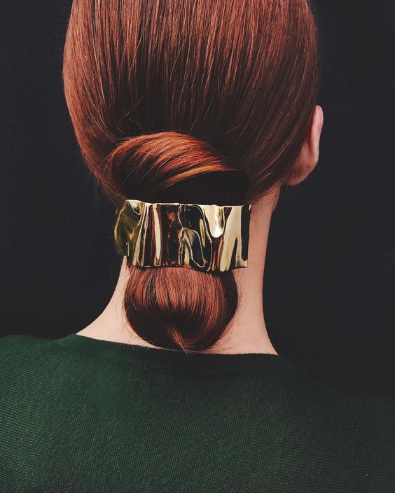 woman with sleek hair gathered into a low chignon with gold ripple accessory