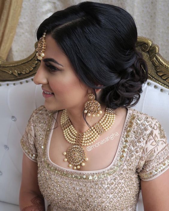 woman with dark hair gathered loosely into curls at the nape of her neck with gold and pearl tikka 