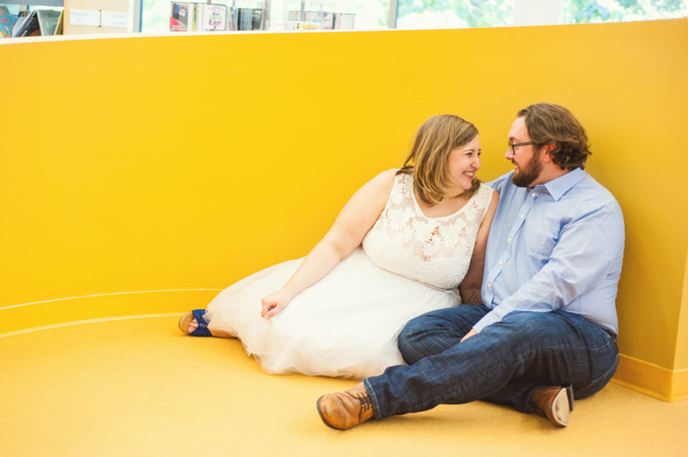 plus size white man and woman looking at each other and laughing in front of a yellow wall