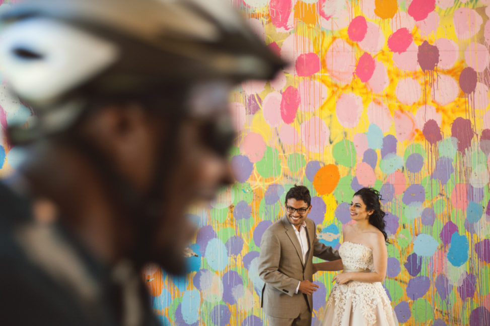 man and women standing in front of a mural wall laughing with a laughing bike messenger riding by in the foreground