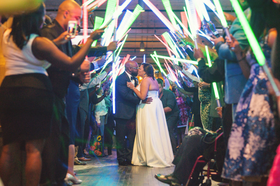 black bride and groom kissing under light saber archway