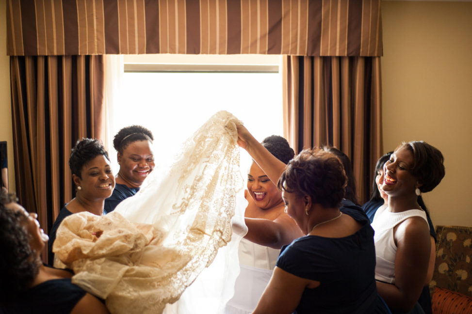 bride surrounded by bridesmaids helping her into dress